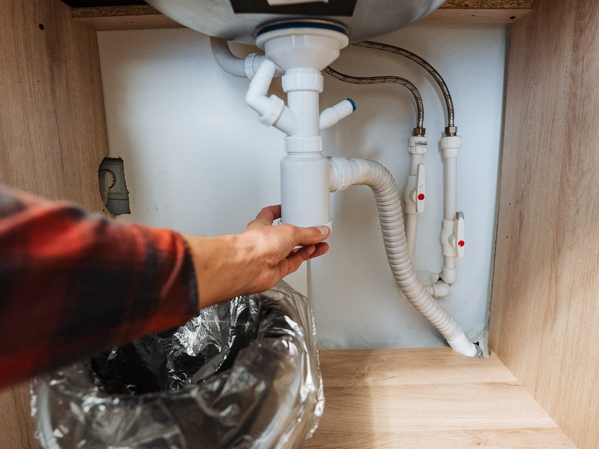 Hands adjusting the waste fitting beneath a kitchen sink