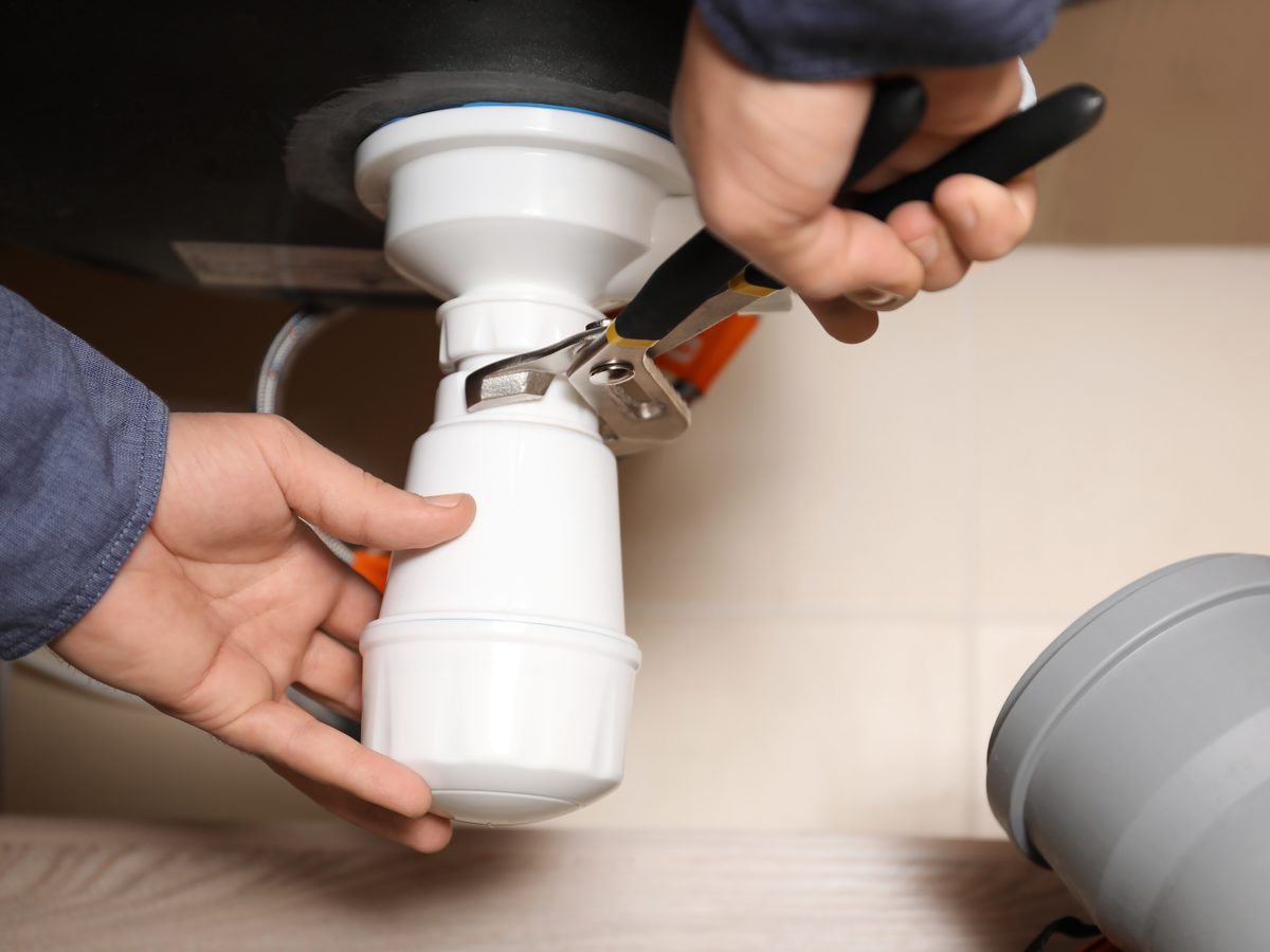 Bottle trap being fitted under a sink with a pair of pliers